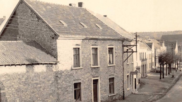 Une vieille maison en pierre dans une rue calme. À l'arrière-plan, plusieurs autres bâtiments et arbres sont visibles.