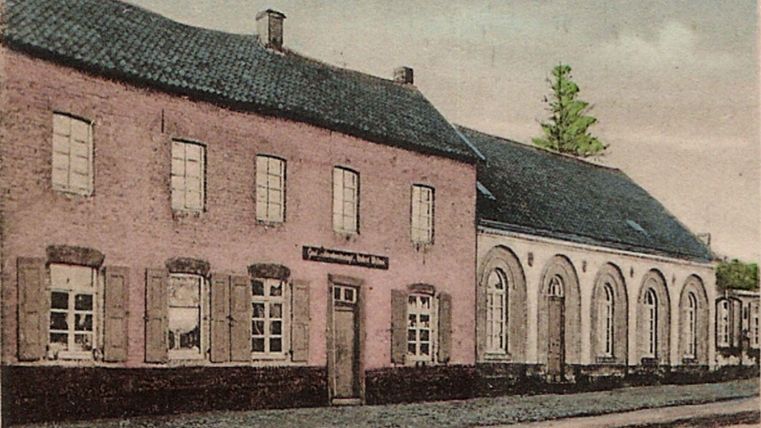Ein altes, charmantes Gebäude mit pinkfarbener Fassade und vielen Fenstern. Daneben steht ein weiterer Anbau mit runden Fenstern und einem dunklen Dach.