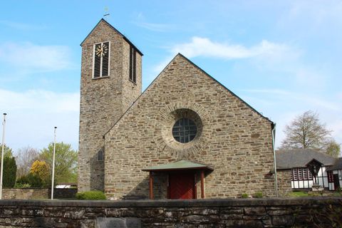 Eine steinerne Kirche mit einem hohen Turm und großen Fenstern. Umgeben von Bäumen und einer ruhigen Landschaft.