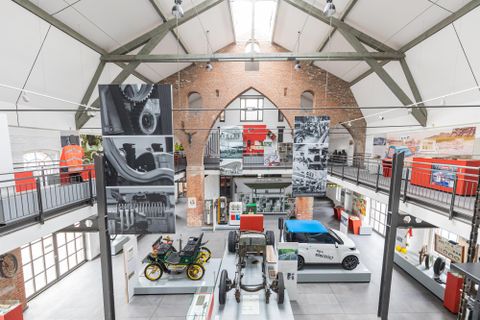 Ein modernes Museum mit historischen Fahrzeugen und großen Wandbildern. Der Raum hat hohe Decken und eine offene Architektur.