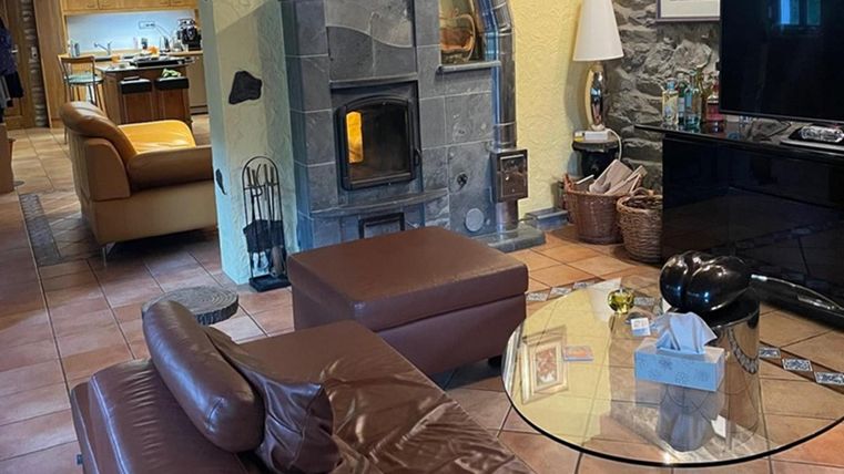 Een gezellige woonkamer met een donkerbruin bank en een ronde glazen tafel. Op de achtergrond is een open ruimte te zien met een moderne keuken en een houtkachel.