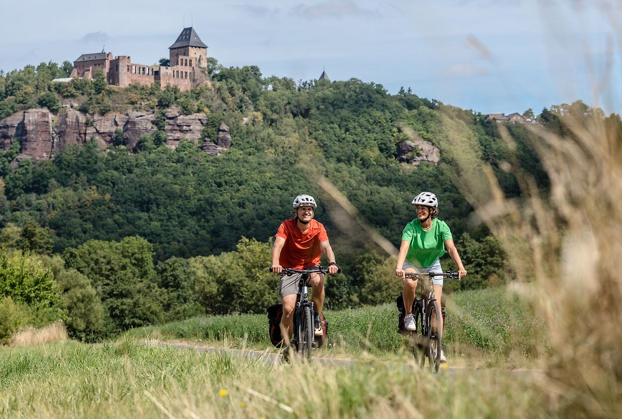 Zwei Personen fahren Fahrrad und im Hintergrund ist die Burg Nideggen zu sehen