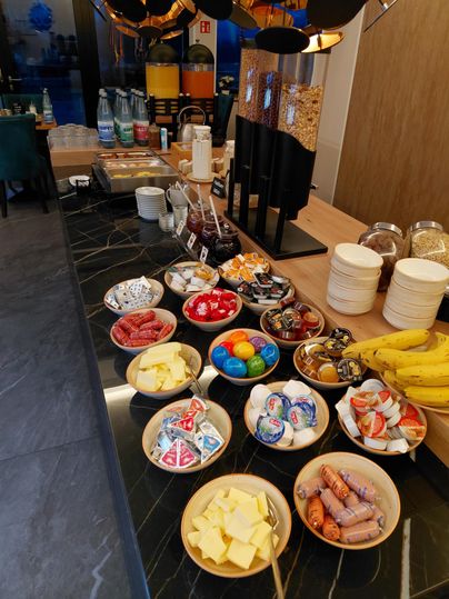 Een buffet met verschillende ontbijt ingrediënten. Er zijn worst, kaas, fruit en snoepjes, evenals dranken.