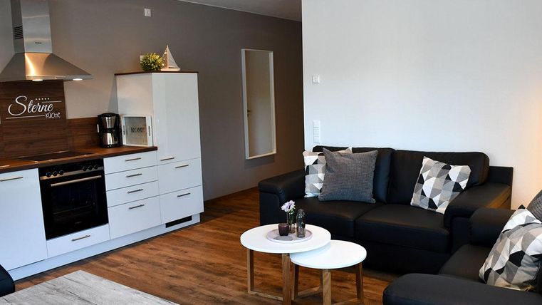 Eine moderne Wohnung mit einer offenen Küche und einem gemütlichen Wohnbereich. Die Möbel sind in neutralen Farben gehalten, mit zwei kleinen Tischen in der Mitte.