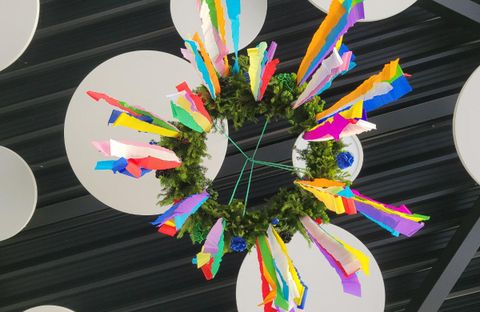 Eine bunte Dekoration mit vielen farbigen Papierstreifen und einem grünen Kranz. Sie hängt von der Decke und bringt Freude in den Raum.