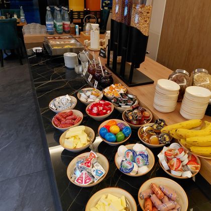 Ein Buffet mit verschiedenen Frühstückszutaten. Es gibt Wurst, Käse, Obst und Süßigkeiten sowie Getränke.