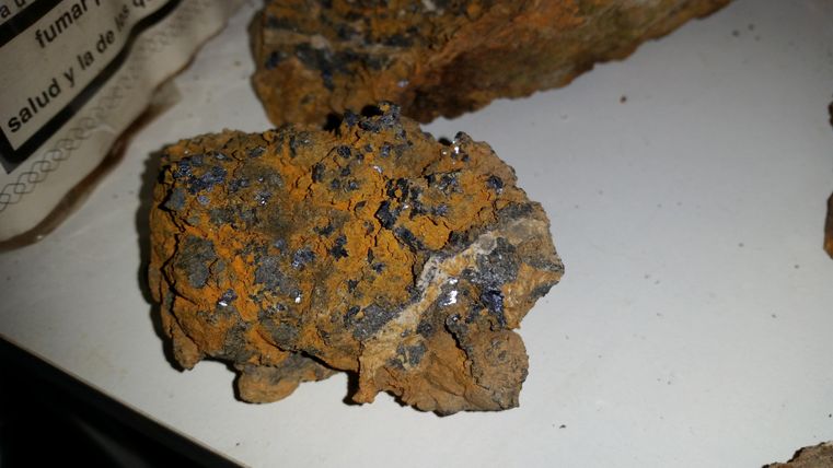 Un morceau de roche avec une surface orange et de petits minéraux scintillants. La structure est rugueuse et irrégulière.