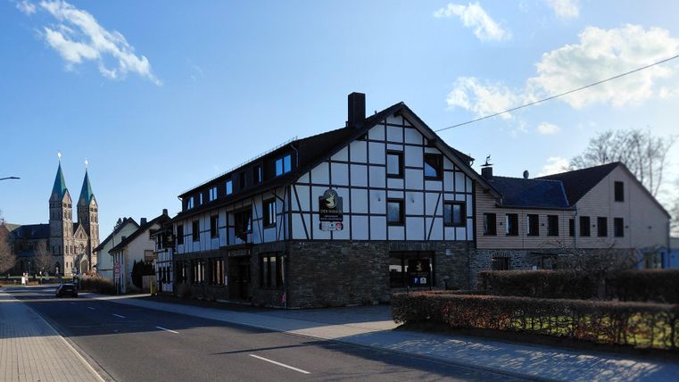 Ein charmantes Fachwerkhaus mit einem Straßencafé. Im Hintergrund sind zwei spitze Kirchtürme sichtbar.