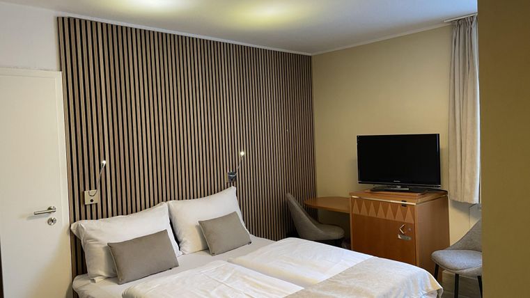 Ein modernes Hotelzimmer mit einem Doppelbett und einer komfortablen Sitzgelegenheit. An der Wand befindet sich ein Fernseher, und die Dekoration ist schlicht und elegant.