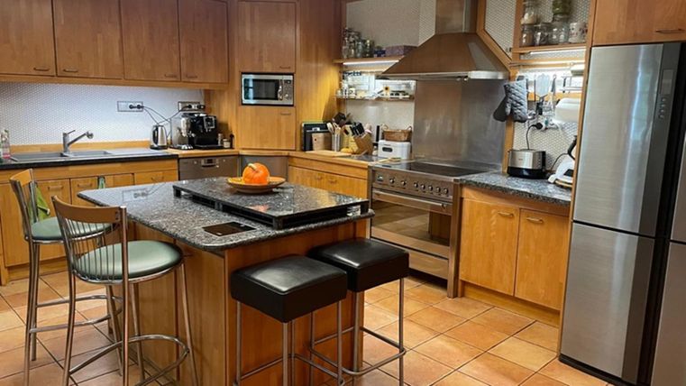 Een moderne keuken met houten meubels en granieten oppervlakken. Op het eiland staat een schaal met een sinaasappel.