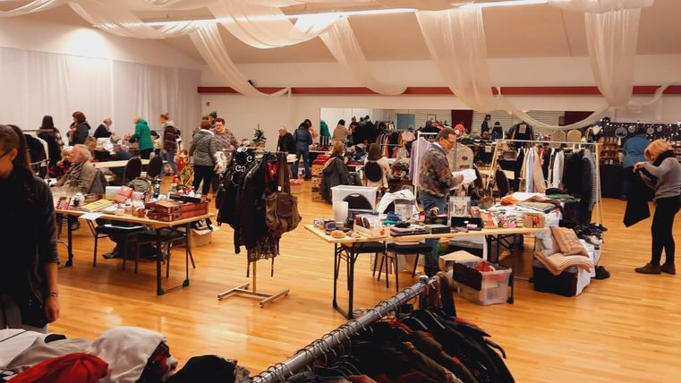 Ein belebter Flohmarkt mit Tischen voll Kleidung und verschiedenen Gegenständen. Viele Menschen stöbern und kaufen in einer gemütlichen Atmosphäre.