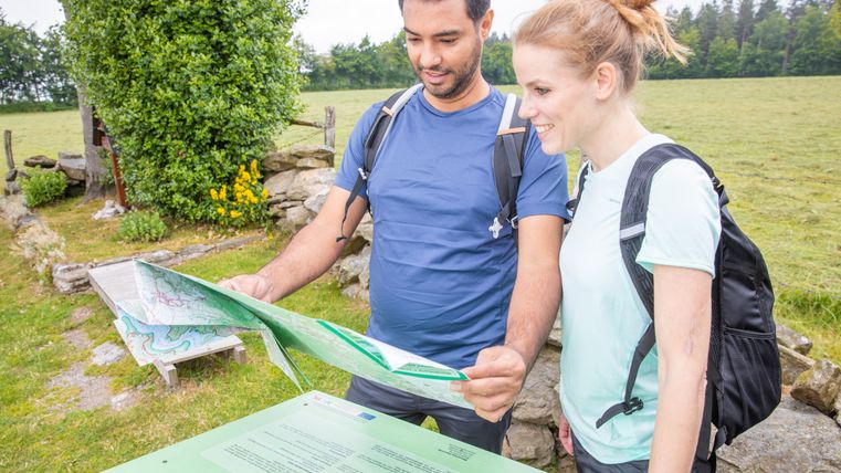 Deux personnes regardent une carte de randonnée à l'extérieur.