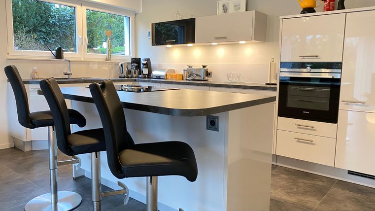 Een moderne keuken met een grote keukeneilandtafel en een hoge stoel in minimalistisch ontwerp. Grote ramen zorgen voor veel natuurlijk licht.