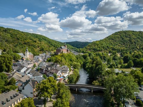 Une ville pittoresque au bord de la rivière, entourée de collines douces et de forêts denses. Les nuages glissent à travers un ciel clair, tandis que l'architecture de la ville incarne une histoire visible.