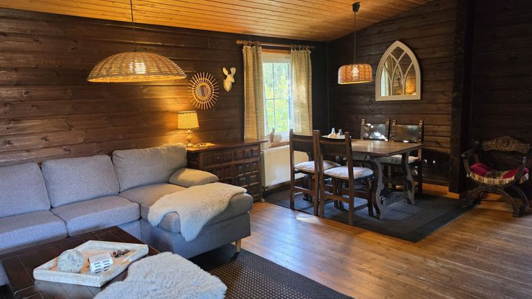 Ein gemütliches Wohnzimmer mit Holzverkleidung, einem bequemen Sofa und einem Esstisch. Große Fenster lassen viel Licht herein und schaffen eine einladende Atmosphäre.
