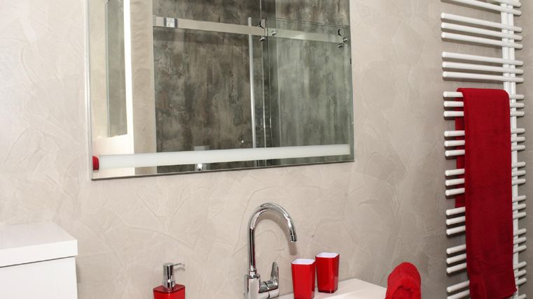 Une salle de bain moderne avec un lavabo blanc et un grand miroir. Des serviettes rouges et des accessoires apportent une touche de couleur au design épuré.