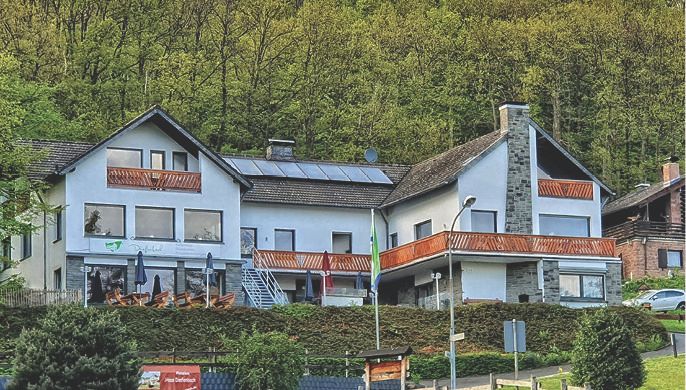 Ein modernes Haus in einer grünen Umgebung, umgeben von Bäumen. Es hat große Fenster und eine Sonnenterrasse.