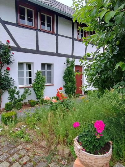 Une maison à colombages traditionnelle avec un jardin bien entretenu. Des fleurs colorées et des plantes vertes décorent l'entrée.