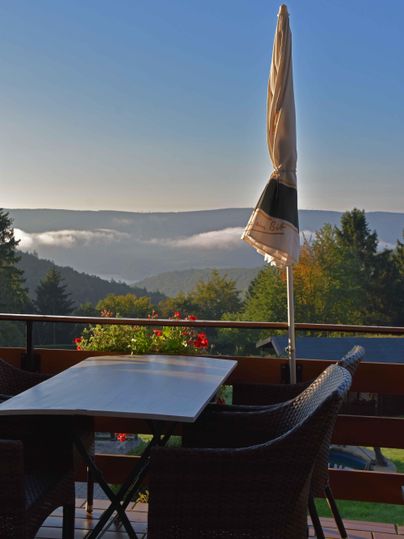 Een gezellige terras met een tafel en stoelen, die uitzicht biedt op het heuvelachtige landschap. Op de achtergrond zijn mist en bomen voor een heldere lucht te zien.