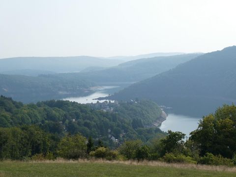A picturesque landscape with gently rolling hills and a river in the background. The sky is lightly cloudy and the vegetation is lush and green.