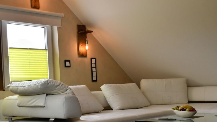 Un salon moderne avec un canapé blanc et une table en verre. La lumière naturelle pénètre par la fenêtre avec des volets jaunes.