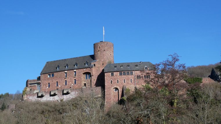 Eine beeindruckende Burg auf einem Hügel mit einem klaren blauen Himmel. Die Architektur ist historisch und rustikal.