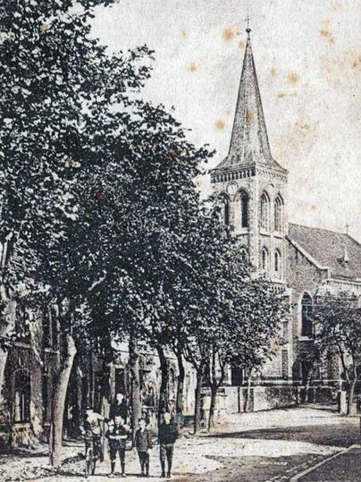 Une vieille rue avec des arbres et un bâtiment d'église en arrière-plan. Plusieurs personnes se promènent près de l'église.