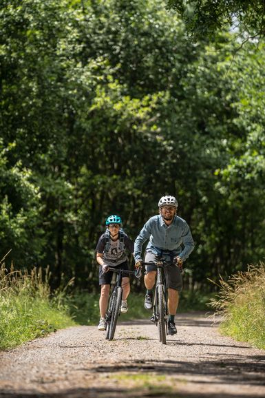 Zwei Mountainbiker fahren hintereinander auf einem befestigten Schotterweg