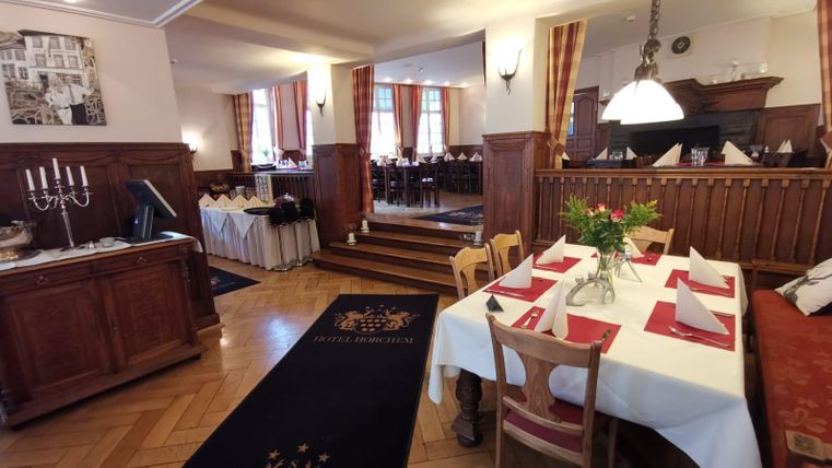 Ein elegantes Restaurant mit Holzinterieur und gedeckten Tischen. Im Hintergrund sind weitere Tische und Fenster mit Vorhängen zu sehen.