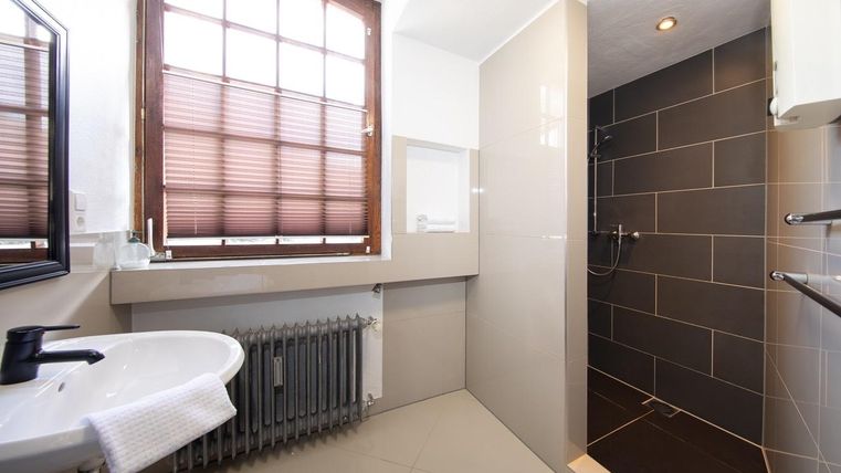 Ein modernes Badezimmer mit einer Dusche und einer weißen Waschbecken. Große Fenster sorgen für viel Tageslicht.