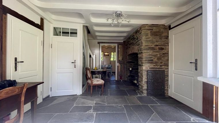 Ein einladender Flur mit Steinboden und einer gemütlichen Atmosphäre. Auf der linken Seite steht ein Tisch mit einem Stuhl, und im Hintergrund ist ein Kamin sichtbar.