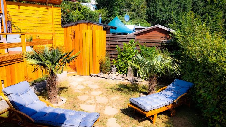 Sauna-Garten! Reserviere Dir die Sauna über unsere Gäste-App Campingplatz Hetzingen und genieße den Aufenthalt im Garten nach dem Saunagang. Ein schöner Garten mit Liegen und Palmen. Die Holzkonstruktion und der grüne Hintergrund schaffen eine entspannte Atmosphäre.