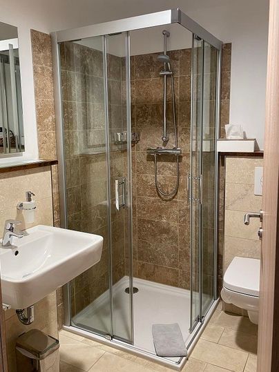 Ein modernes Badezimmer mit einer Glaskabine für die Dusche. Es gibt ein Waschbecken und eine Toilette, umgeben von eleganten Fliesen.